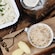 A wood table featuring food in a skillet and a dish, potato shavings, a salt shaker and powder in a sifter